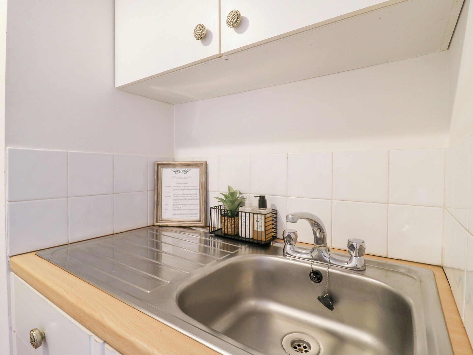 A kitchen with a stainless steel sink, white tiles, and wooden countertops.