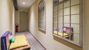 Ein schmaler Flur mit einem Brandschutztürschild, einem Fenster mit einem Rauchverbotsschild und einer hölzernen Bank mit einem gelben Kissen.