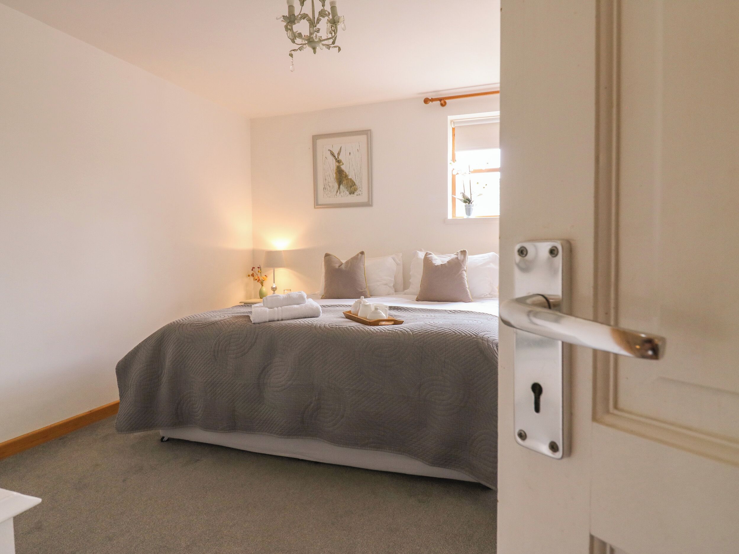 A bedroom with a bed, pillows, a bedside table with a lamp, a framed picture on the wall, and a door with a keyhole.