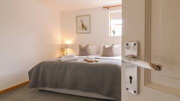 A bedroom with a bed, pillows, a bedside table with a lamp, a framed picture on the wall, and a door with a keyhole.