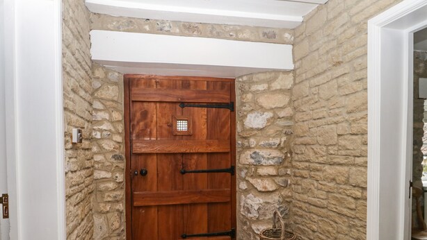 A wooden door with a metal handle, set in a stone wall corridor with a tiled floor. - The Linhay (Axminster)