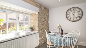 A dining area with a stone wall, a large clock, and a table set for two. - The Linhay (Axminster)