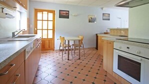 A kitchen with wooden cabinets, a tiled floor, a dining table with chairs, and a stove. - Cozy Village Retreat with Private Pond, Terrace, and Family Amenities in Le Ménil (Le Menil)