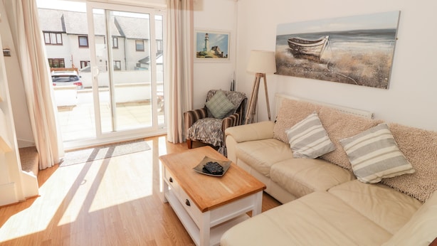 A living room with a sofa, a coffee table, and a painting of a boat on the wall. - Ketch Cottage (Holyhead)