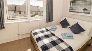 A bedroom with a bed, a window with curtains, a radiator, and a framed picture on the wall. - Ketch Cottage (Holyhead)