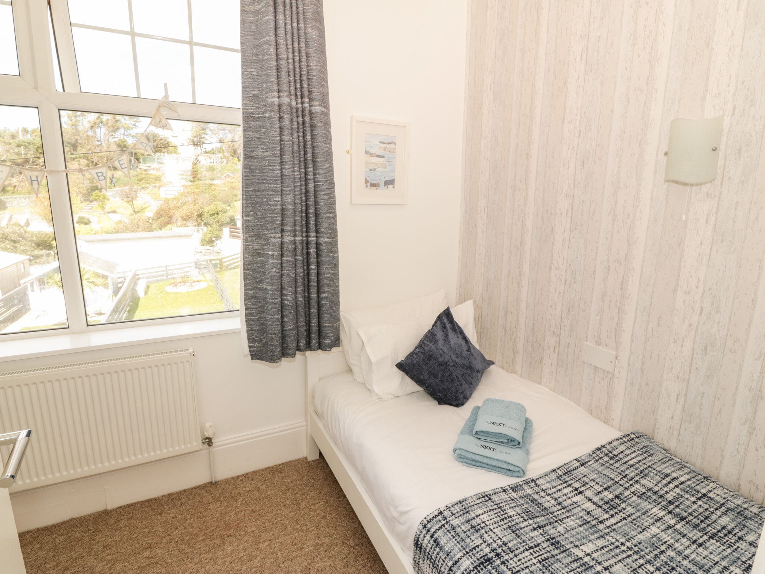 Un dormitorio con cama, ventana con cortinas, radiador y vistas al exterior.
