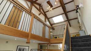 A spacious interior with a wooden staircase, a skylight, and a chandelier. - Snave Barn (Skipton)