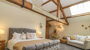 A bedroom with a large bed, a sofa, a dresser, and a chandelier. - Snave Barn (Skipton)