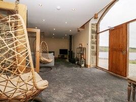 A cozy room with a hanging chair, a sofa, a fireplace, and a large window overlooking a body of water.