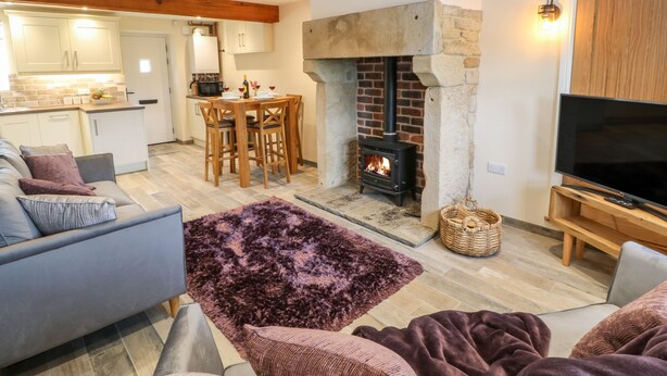 A cozy living room with a fireplace, a TV stand, and a dining area with a table and chairs. - Mirk Cottage (Hebden Bridge)