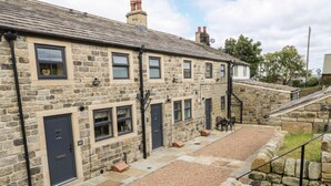 A stone building with multiple doors and windows, a gravel courtyard, and a staircase leading up. - Mirk Cottage (Hebden Bridge)