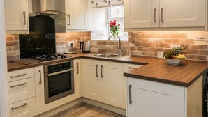 A modern kitchen with white cabinets, a stainless steel range, and a wooden countertop. - Mirk Cottage (Hebden Bridge)