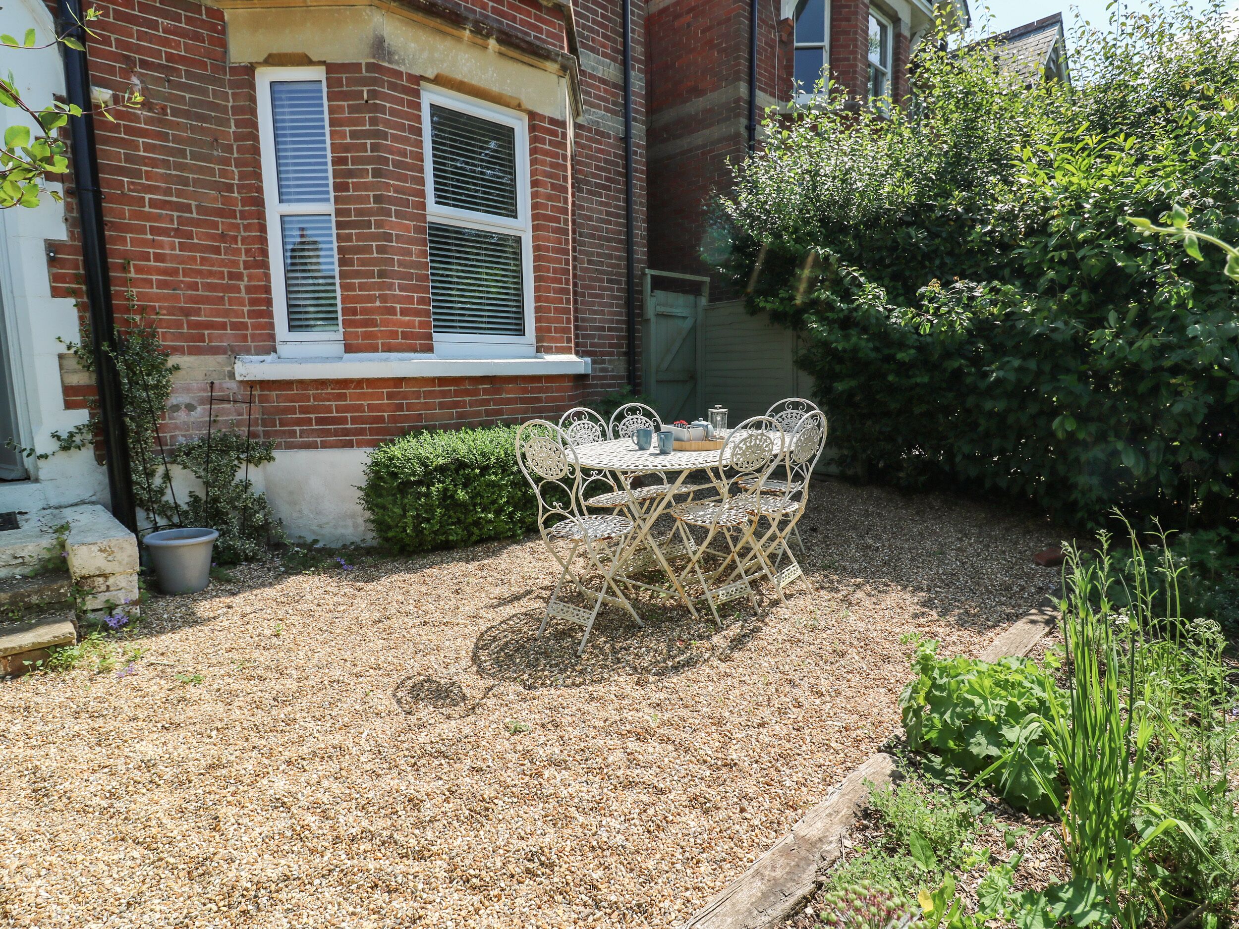 A garden with a metal table and chairs, a brick house, and a hedge.