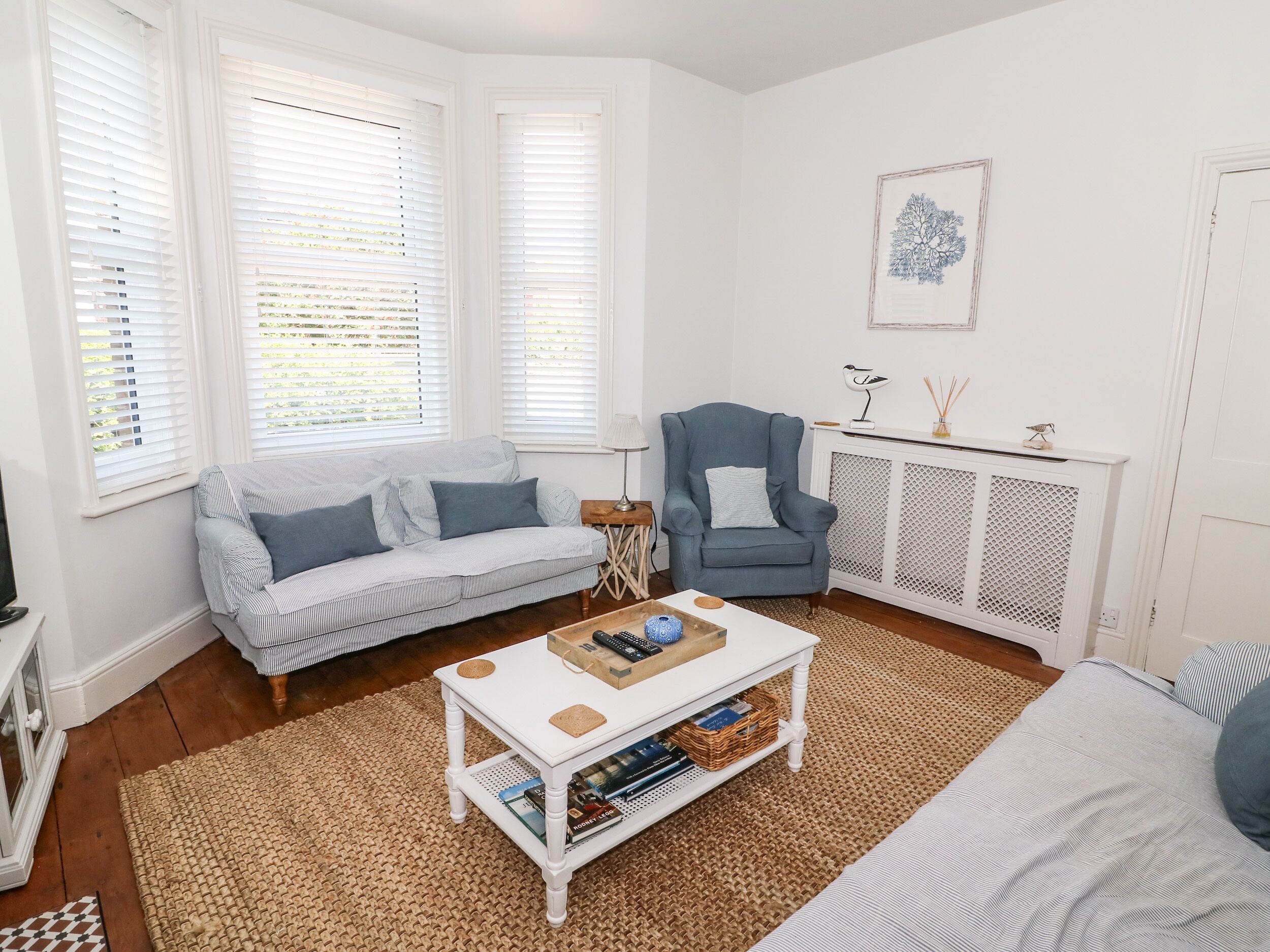 A cozy living room with a striped sofa, a blue armchair, and a white coffee table with books and decorative items.