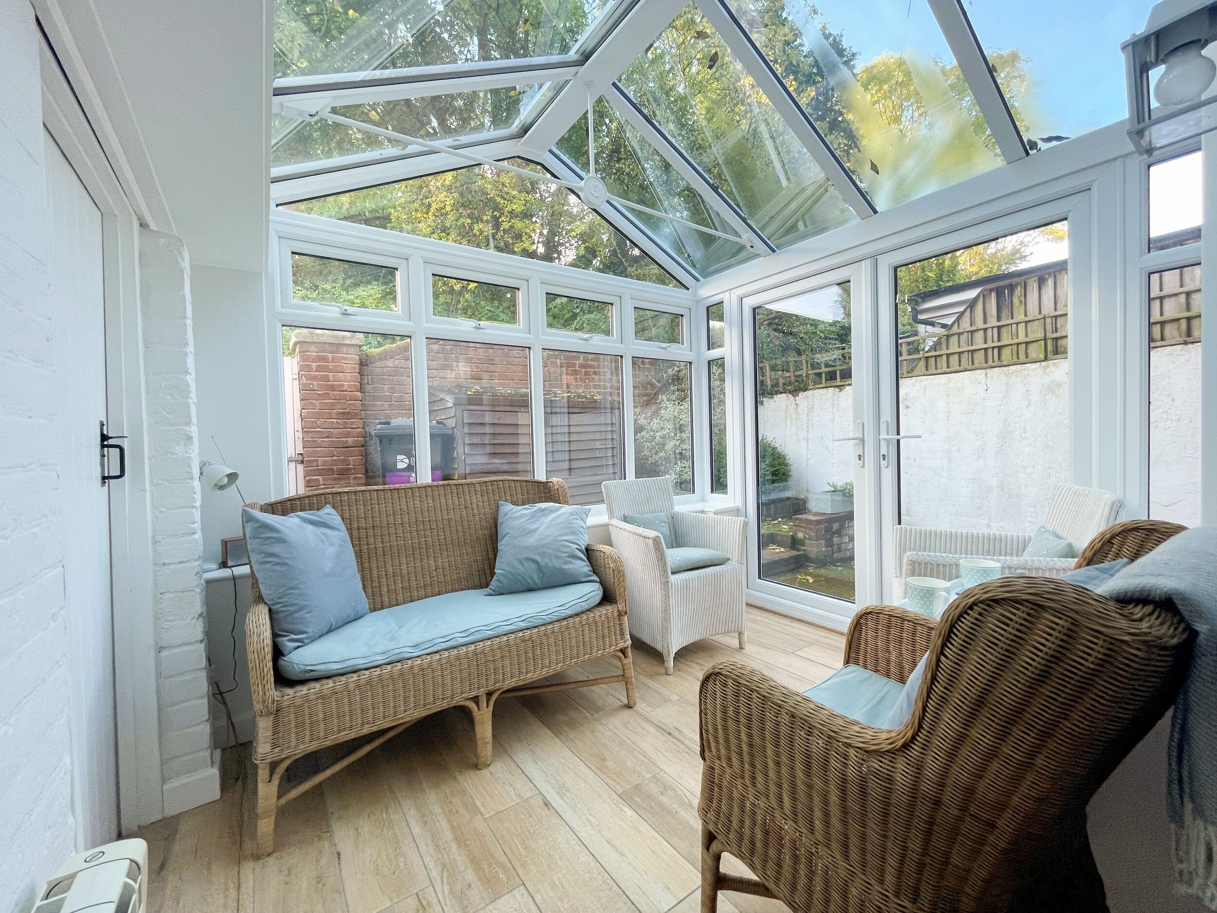 A conservatory with wicker furniture and a glass ceiling, offering a view of the garden.