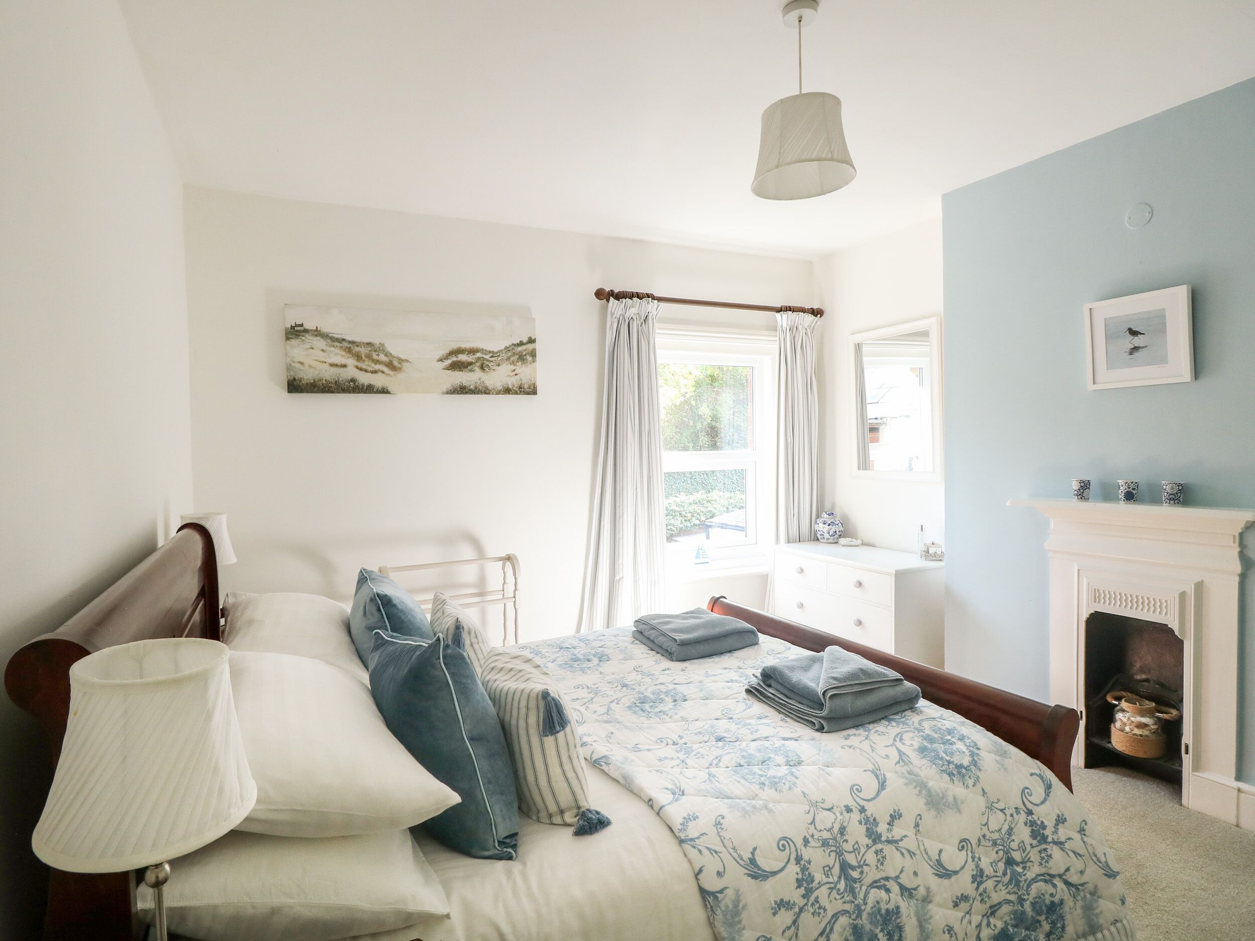 Un dormitorio con cama, lámpara de noche, cómoda, espejo y chimenea.