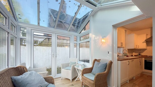 A bright, open-plan living area with a glass ceiling, wicker furniture, a dining table, and a kitchen. - Elm Villa (Wareham)