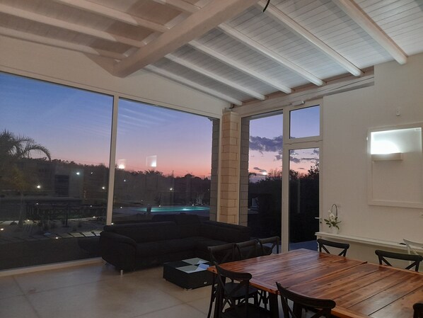 A spacious living area with a large window, a wooden dining table, and a black sofa.
