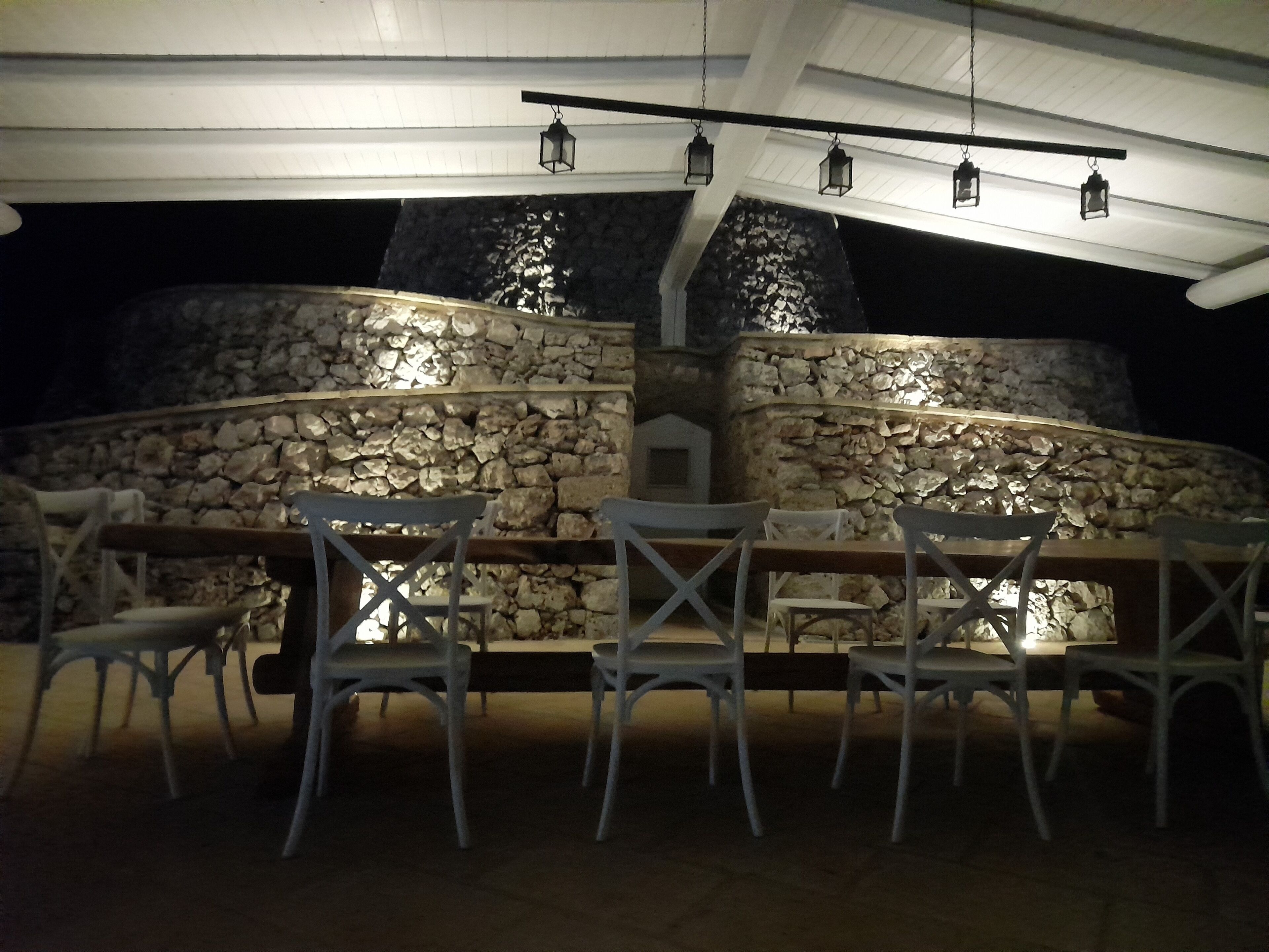 Un área de comedor al aire libre con paredes de piedra y faroles colgantes.