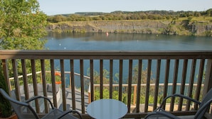 Uma varanda com vista para um lago, uma mesa e duas cadeiras.