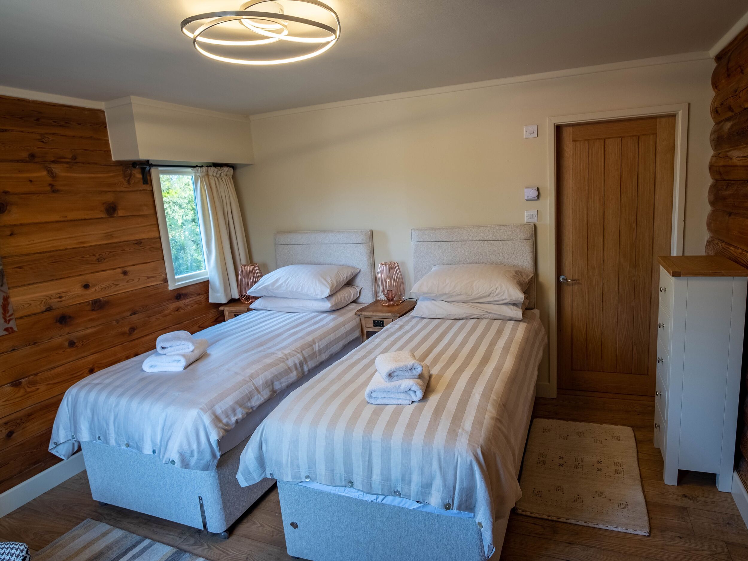 A room with two beds, a wooden wardrobe, and a window with curtains.