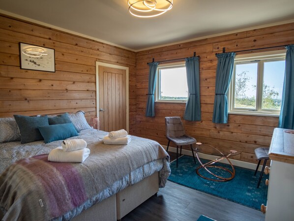 A cozy room with a wooden wall, a bed with pillows, a chair, and a table with a glass top.