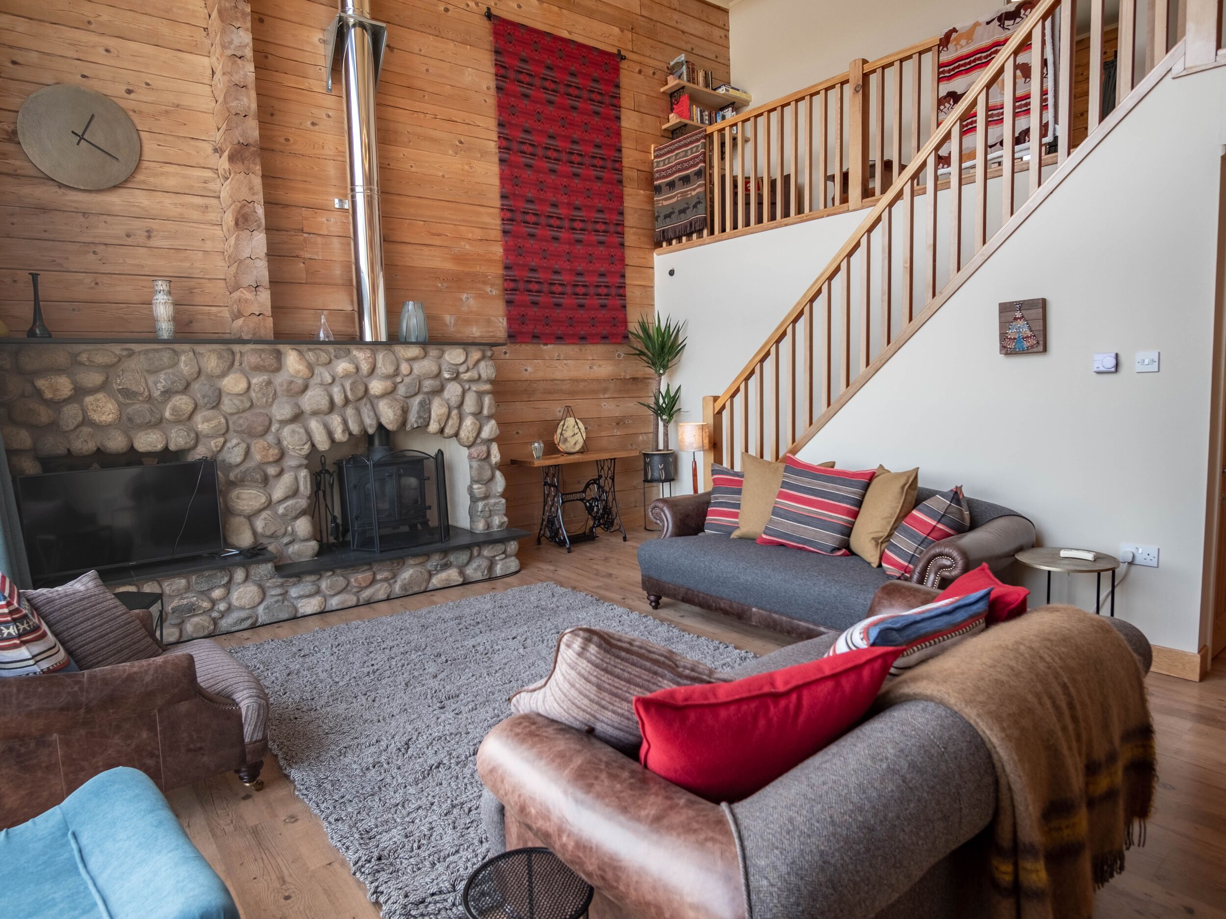 Ein gemütliches Wohnzimmer mit Kamin aus Stein, Holzwänden, einer Treppe und einer bequemen Sitzecke.