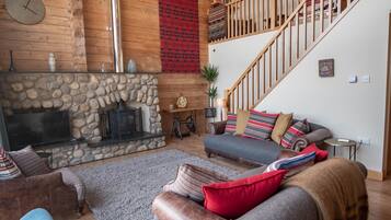 Ein gemütliches Wohnzimmer mit Kamin aus Stein, Holzwänden, einer Treppe und einer bequemen Sitzecke.