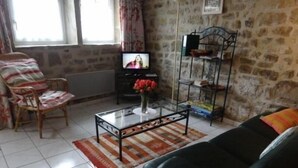 Een woonkamer met een zwarte leren bank, een glazen salontafel met een vaas rode bloemen, een kamerkleed met dessin en een stenen muur.