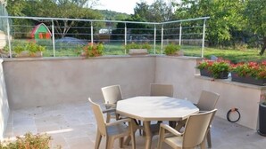 Een terras buiten met een ronde tafel en vier stoelen, omringd door potplanten en uitzicht op een groen landschap.