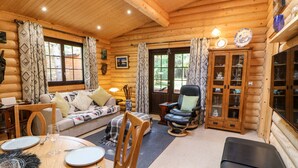 A cozy log cabin interior with a dining area, a sofa, a rocking chair, and a cabinet with glass doors. - Jalan End (Morpeth)