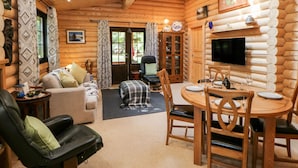 A log cabin interior with a living area, dining table, and a TV mounted on the wall. - Jalan End (Morpeth)