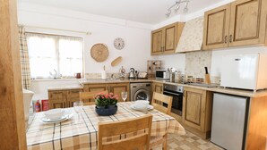 Una cocina con armarios de madera, microondas, refrigerador y una mesa de comedor con sillas.