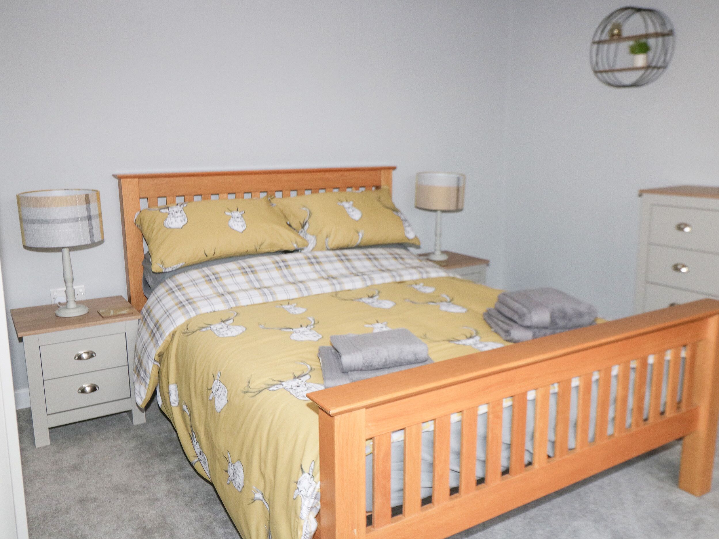 A bedroom with a wooden bed, two bedside tables, a nightstand, and a wall-mounted shelf.