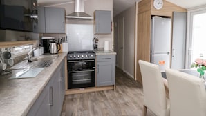 A compact kitchen with a stove, oven, microwave, and sink. There is a dining area with a table and chairs. - Ystwyth 26 (Borth)