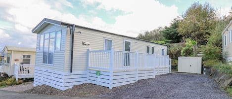 A mobile home with a fenced deck, a small attached garage, and a gravel driveway.