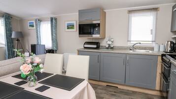 A modern kitchen with grey cabinets, a microwave, and a coffee maker. There is a dining table with black placemats and a vase of flowers.