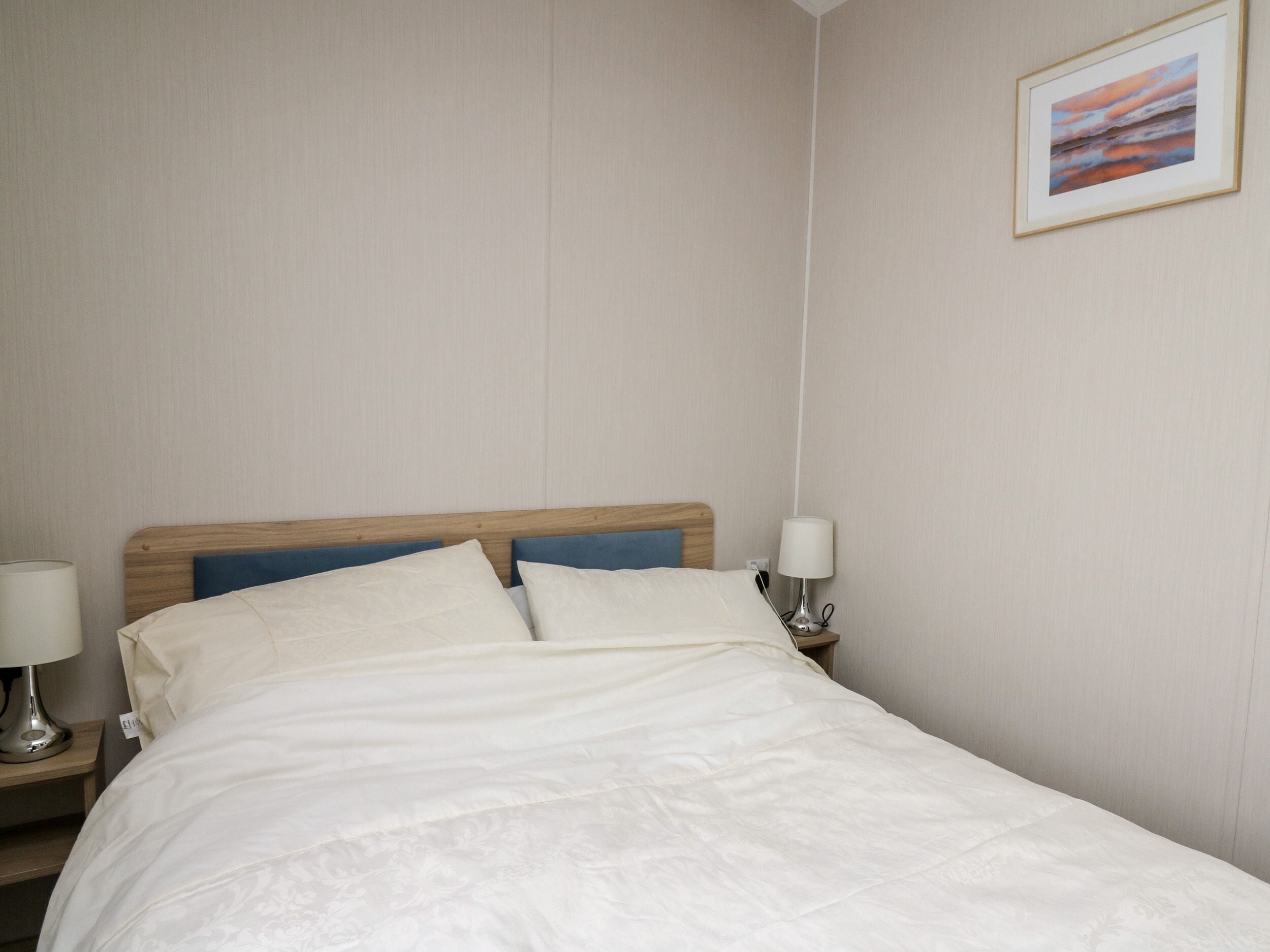 A neatly made bed with a wooden headboard, two bedside lamps, and a framed picture on the wall.