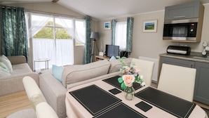 A cozy room with a sofa, a dining table with placemats, a kitchen area with a microwave, and a TV. - Ystwyth 26 (Borth)