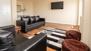 A modern living room with a black leather sofa, a coffee table, and a TV mounted on the wall. - The Beach House (Thornton-Cleveleys)