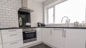 A modern kitchen with white cabinets, a stainless steel oven, and a black countertop. - The Beach House (Thornton-Cleveleys)