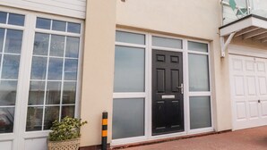 A residential building with a black front door, white-framed windows, and a balcony with a glass railing. - The Beach House (Thornton-Cleveleys)