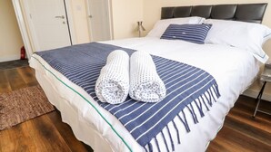A neatly made bed with a striped bedspread, two rolled towels, and a bedside lamp. - The Beach House (Thornton-Cleveleys)