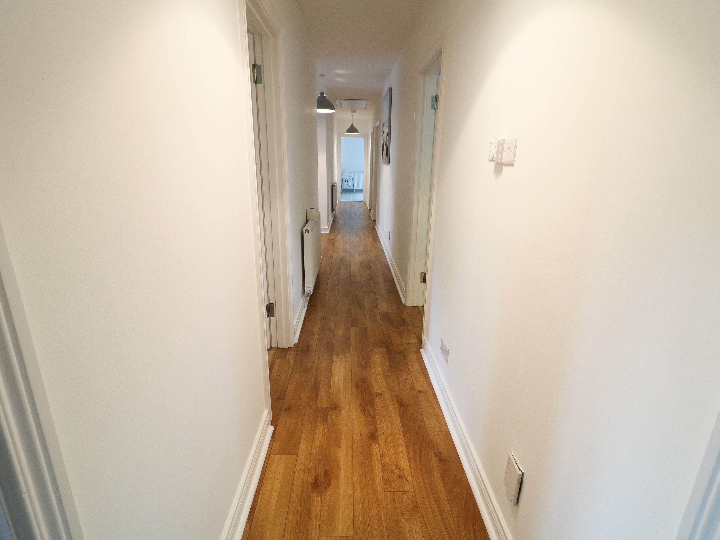 A narrow hallway with wooden flooring and white walls.