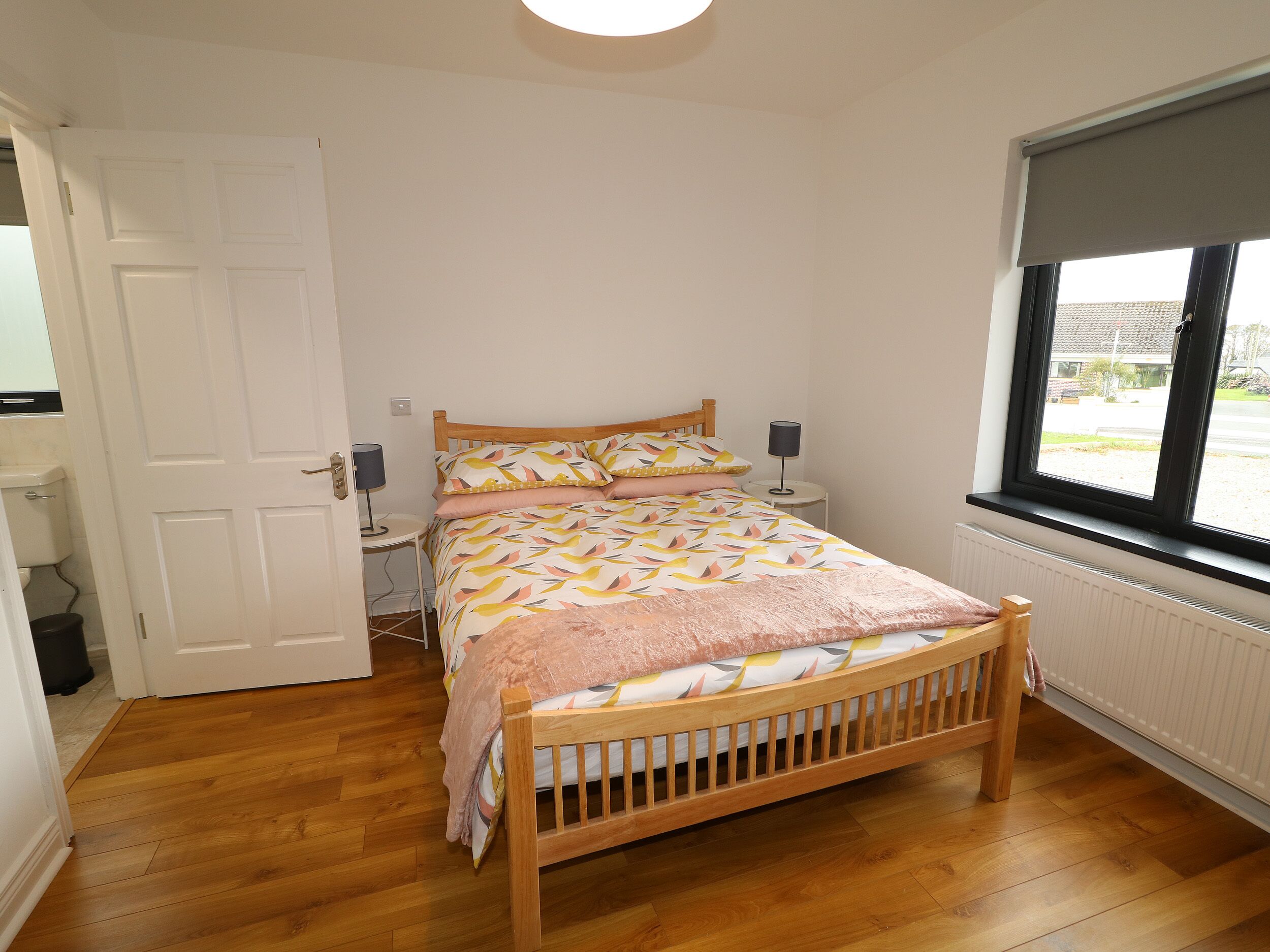 Un dormitorio con cama de madera, una mesita de noche con lámpara, una ventana con vistas y un radiador.