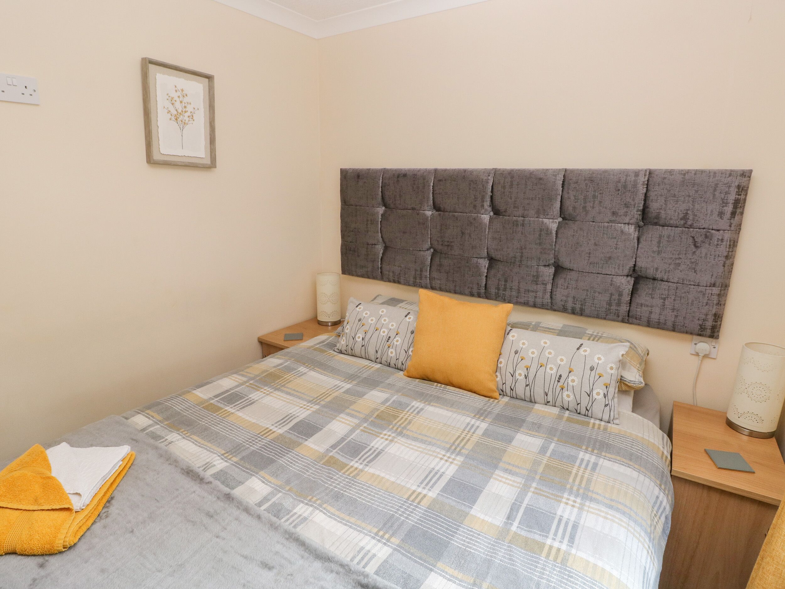 A bedroom with a large bed, a headboard, two bedside tables, and a wall-mounted light fixture.