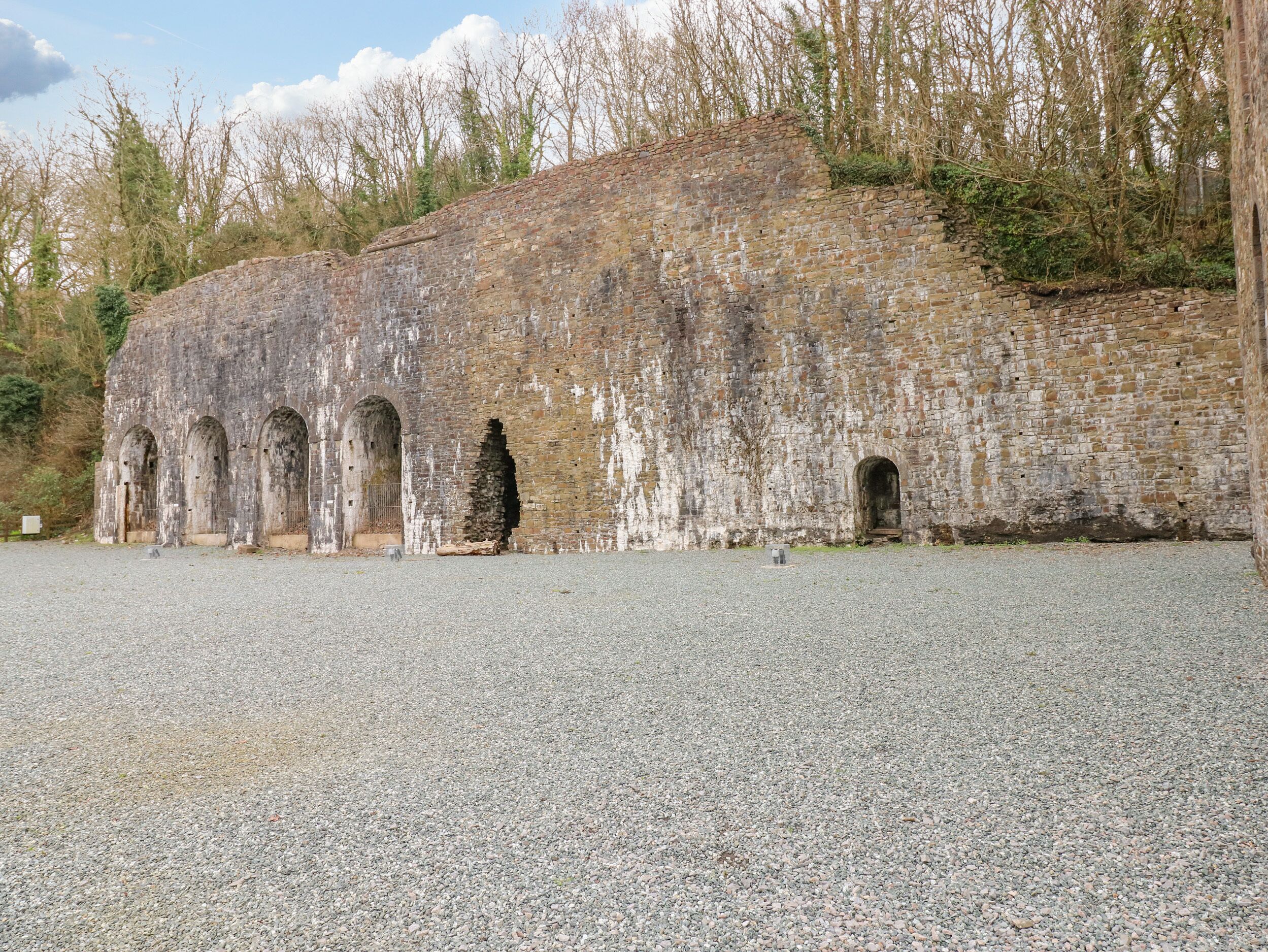 A historic stone building with multiple arched doorways and a gravel ground.