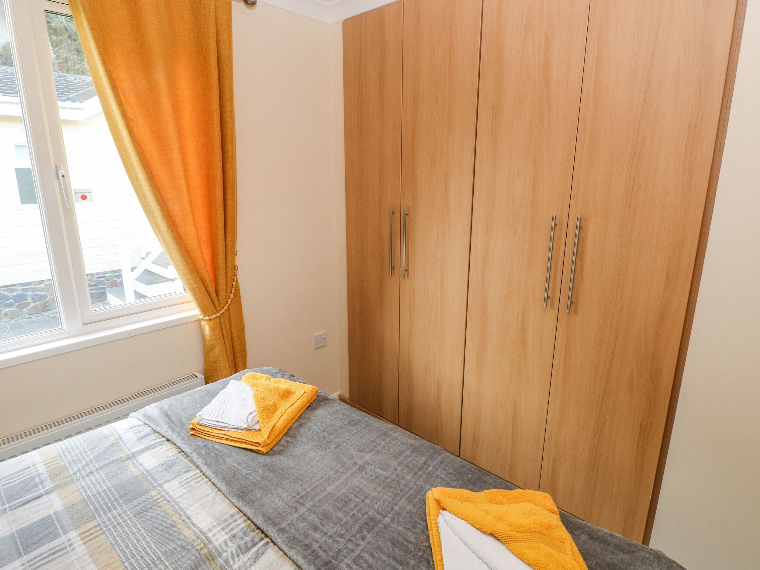 A bedroom with a bed, a window with curtains, and wooden wardrobes.