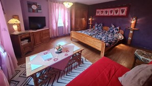 A bedroom with a bed, a TV, a desk, and a dining table.