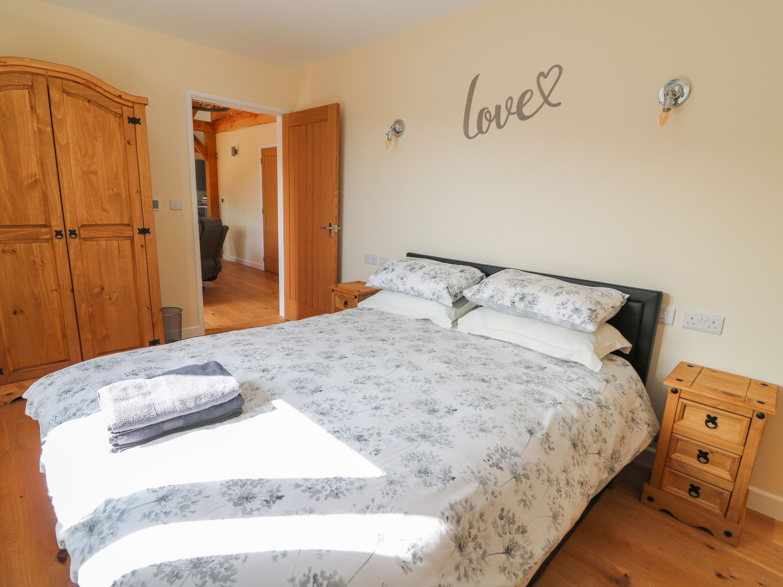 A bedroom with a bed, wooden wardrobe, and a wall with a 'love' sign.